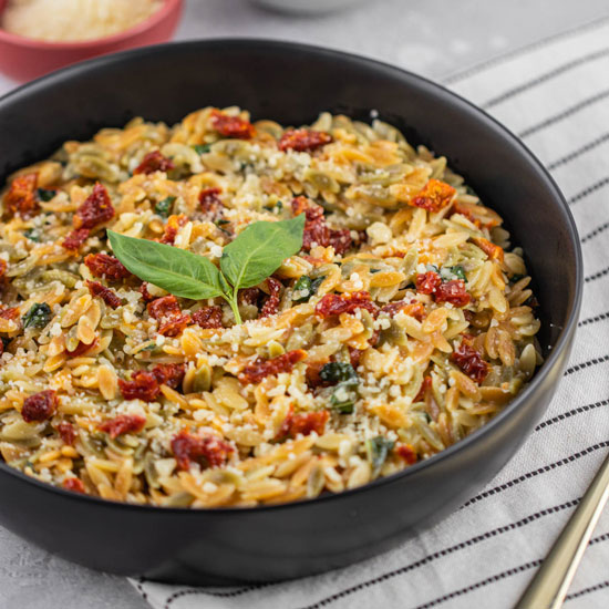 One-Pan Orzo with Sun-Dried Tomato and Mascarpone Recipe in Black serving bowl, with parmesan cheese