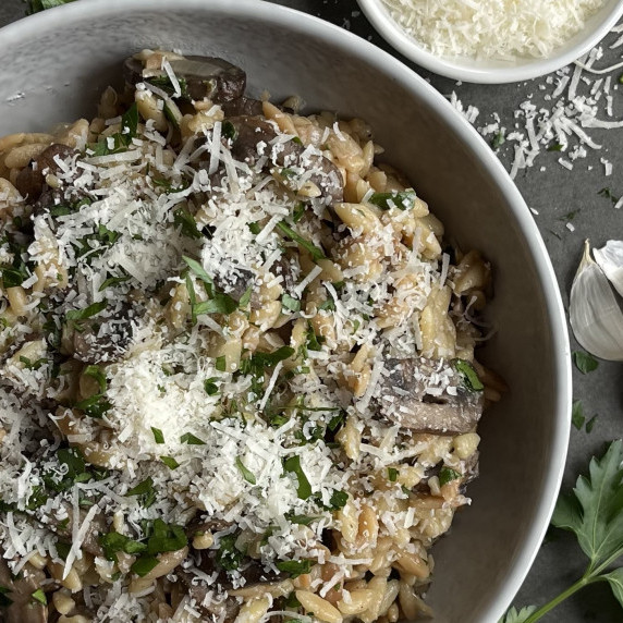 Orzo and sauteed mushrooms in a grey bowl garnished with parmesan cheese and fresh parsley.