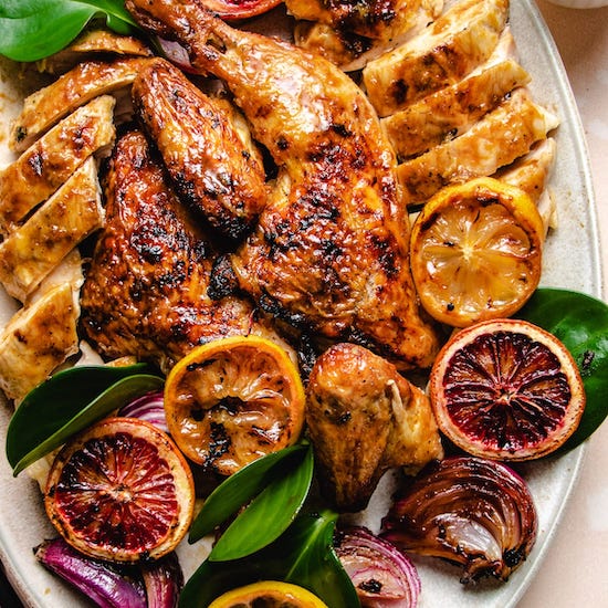 Sliced roasted chicken lemons and oranges with green leaves arranged on a white plate