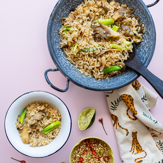 A small  wok and bowl with Thai fried rice on a soft pink background.