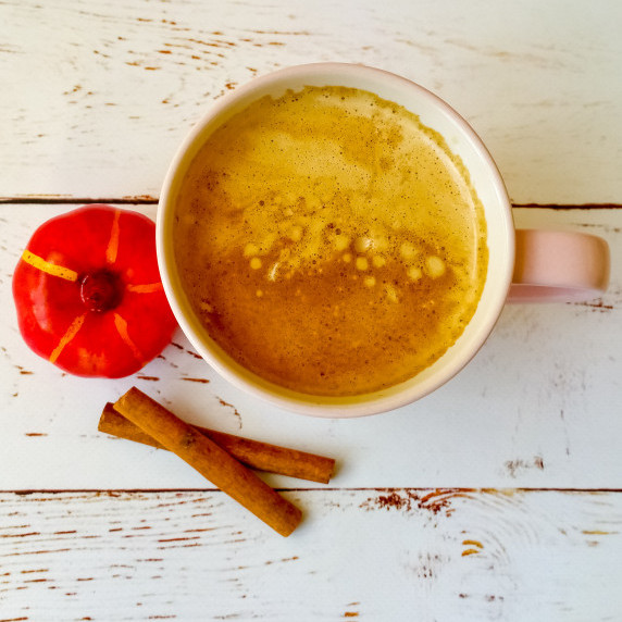 Cup of pumpkin spice latte, next to a small pumpkin and cinnamon sticks.