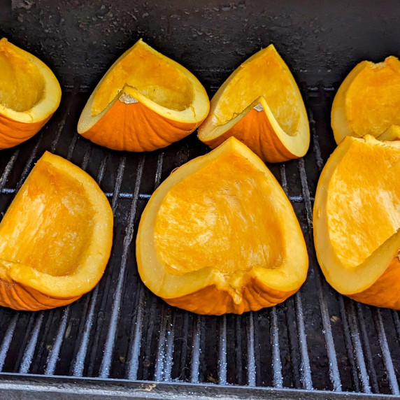 Pumpkin quarters smoking on a smoker. 