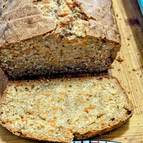 A loaf of carrot muffin bread sliced on a wooden cutting board. 