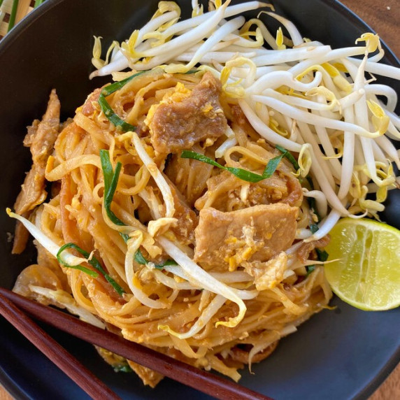 Pad Thai noodles with bean sprouts and meat on top, a piece of lime, and wooden chopsticks.