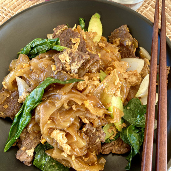 Pad see ew with beef on a black dish with wooden chopsticks.