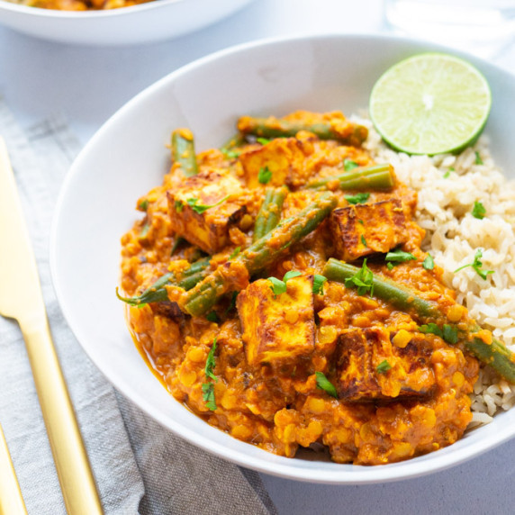 Paneer vegetable curry with red lentils & green beans in a white bowl served with rice.