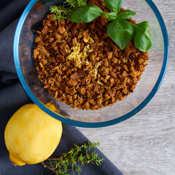 A bowl of crispy Pangrattato with Herbs and Lemon Zest, surrounded by lemon and herbs.