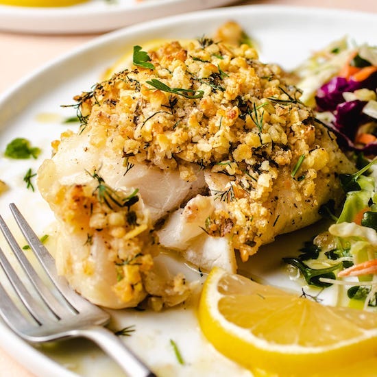 Baked cod with panko topping, sliced lemon and multicolor slaw on a white plate with fork