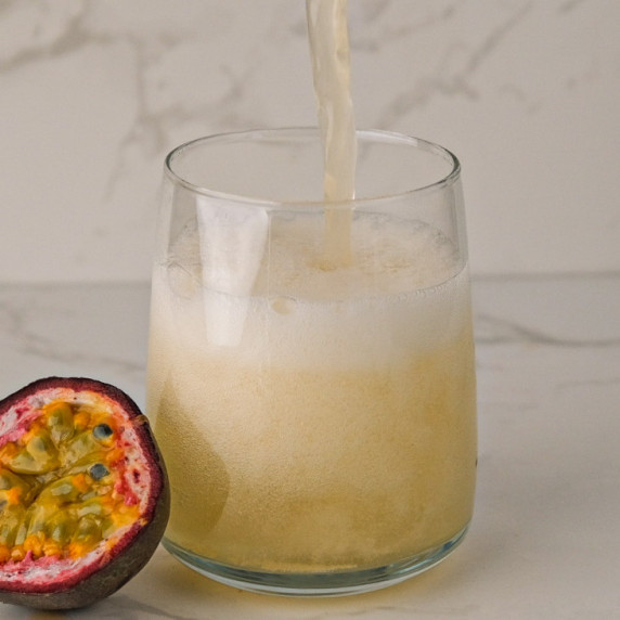 Kombucha being poured into a glass with half a passion fruit next to it