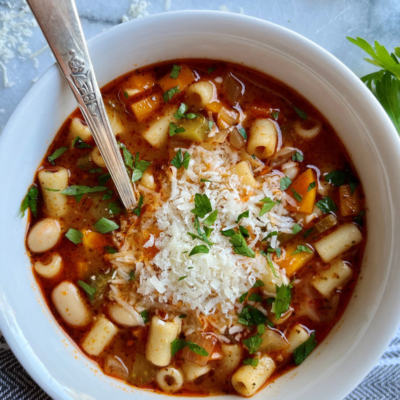 Pasta and bean soup topped with grated cheese and parsley in a white bowl.