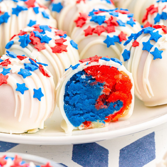 Close up of the inside of a red and blue cake ball next to more cake balls on a plate.