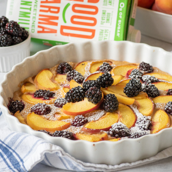 Clafoutis in a tart pan topped with peach slices and blackberries, adn dusted with powdered sugar