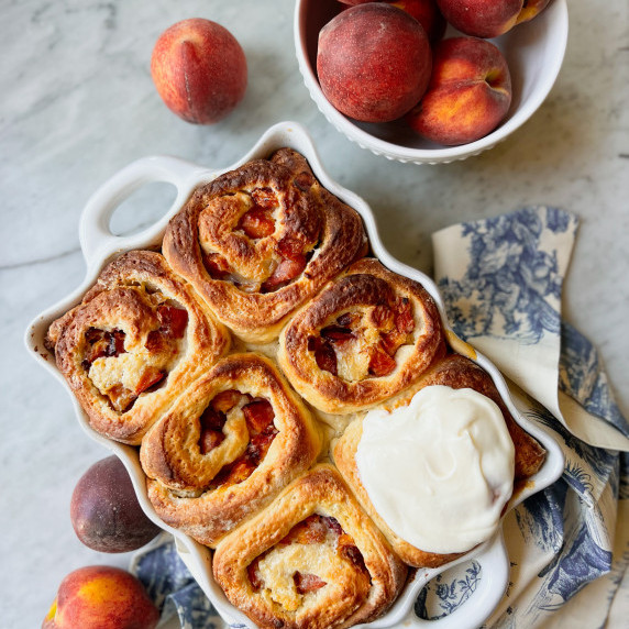 peach cobbler rolls with cream cheese frosting and a bowl of peaches