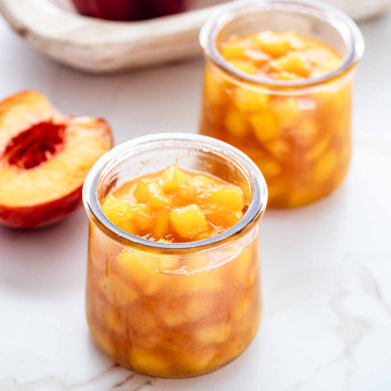 Two jars of peach compote on a marble surface
