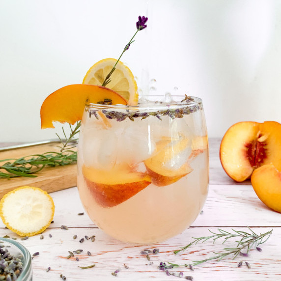 peach lavender lemonade spritzer with a splash and fresh garnishes of peaches, lavender, and lemon