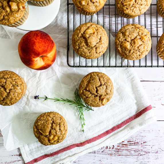 peach muffins on a dish towel and cooling rack with a peach and a sprig of lavender
