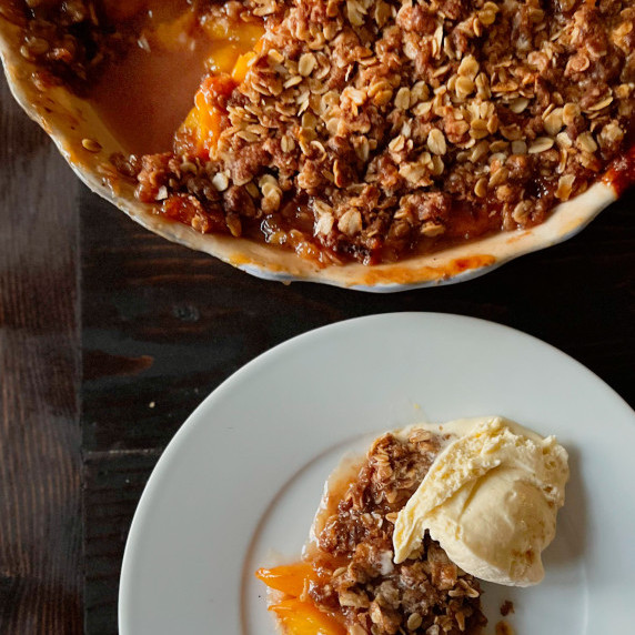 Peach Pie Crumble with a serving on a plate with vanilla ice cream.