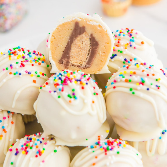 Peanut butter truffles with sprinkles with one cut so you can see a peanut butter cup inside.