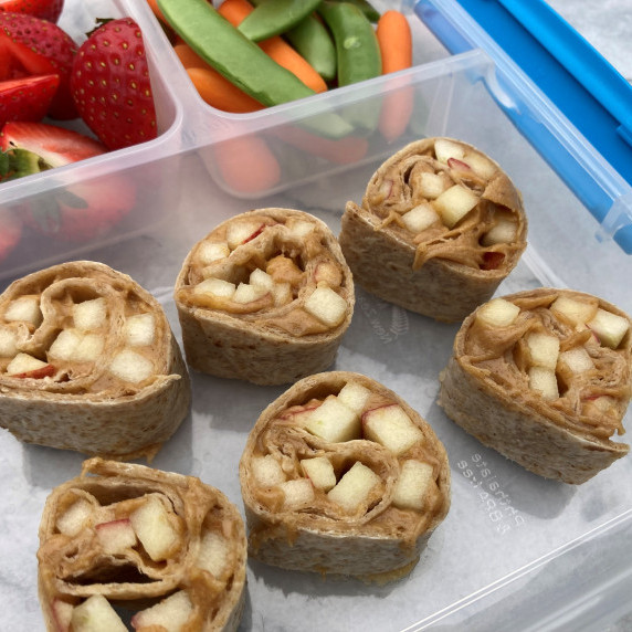 Peanut butter and apple wrap in a bento box with strawberries, snap peas and baby carrots.