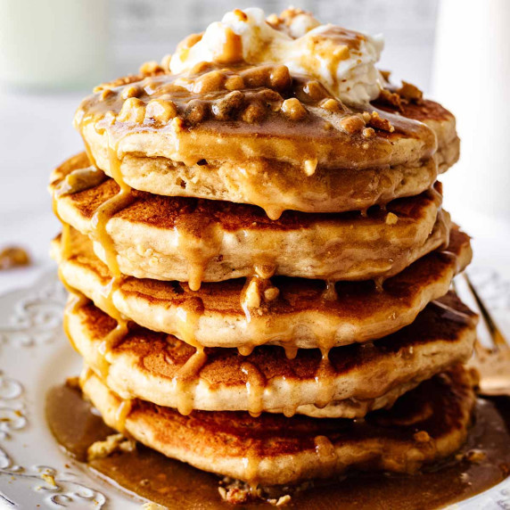 Stack of peanut butter pancakes topped with peanut butter syrup and whipped cream