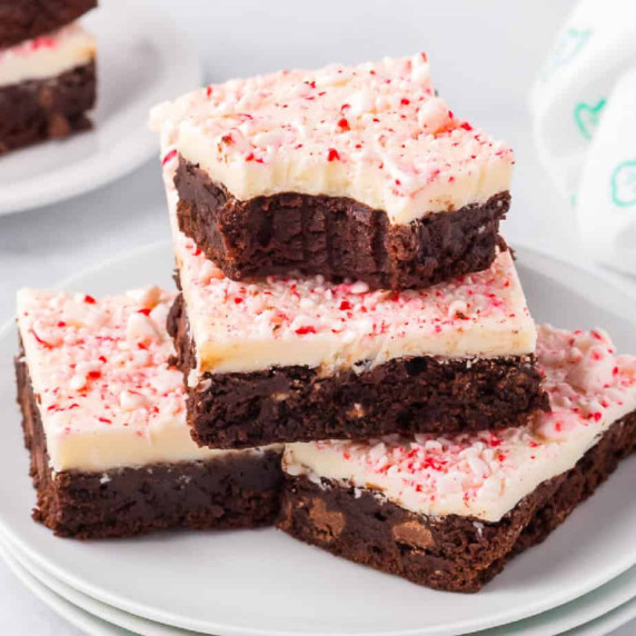 Brownies topped with white chocolate and pieces of peppermint stacked in a pile on a plate.