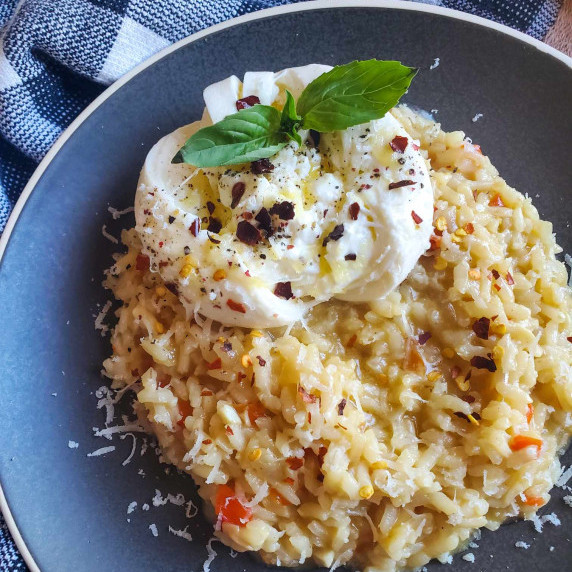 Creamy risotto with a white nest of burrata on top. Served on a grey plate with a checkered towel.