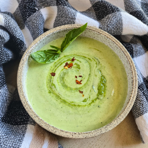 A bowl of green pesto aioli, fresh green basil, pops of red against a checkered towel.