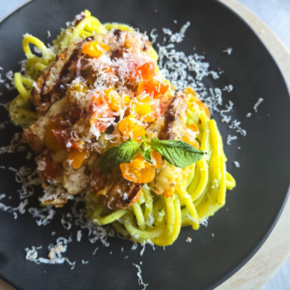 A nest of vibrant green pasta topped with golden brown chik'n and fresh bruschetta topping.