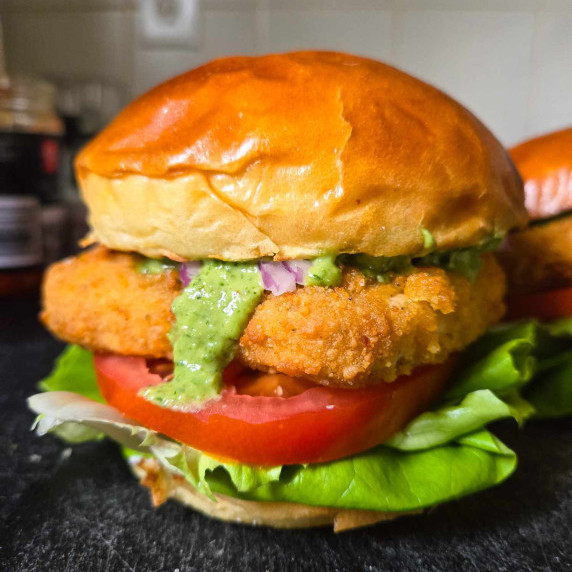 Golden brown brioche buns, green pesto, red tomatoes, lettuce, and a golden brown patty.