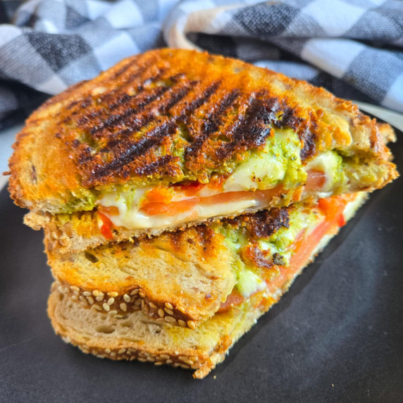 Gorgeously golden grilled sandwich with pops of red & green on a black plate.