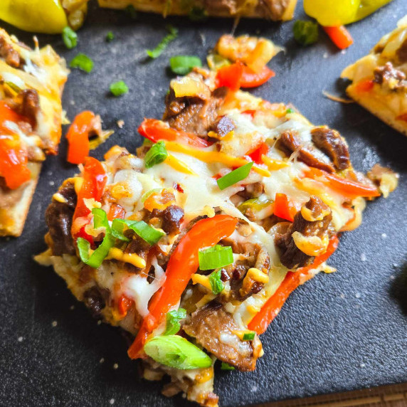 Squares of Philly Cheesesteak Flatbread on a black cutting board.