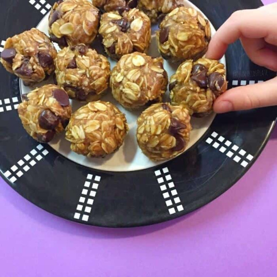 Close up of a child's hand taking a chocolate chip snack bite from a plate.