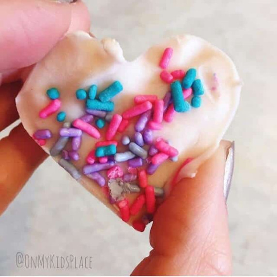 A hand holding a frozen yogurt treat shaped like a heart topped with sprinkles.