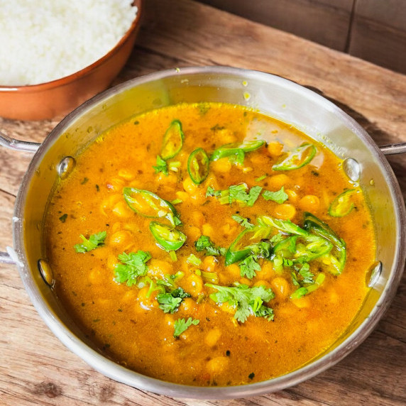 Split chickpea curry arranged in silver wok placed on wooden table