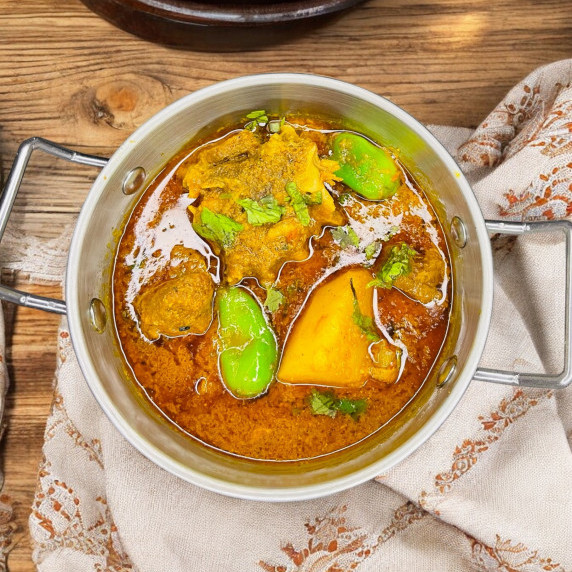 Aloo gosht arranged in silver bowl places on printed linen 