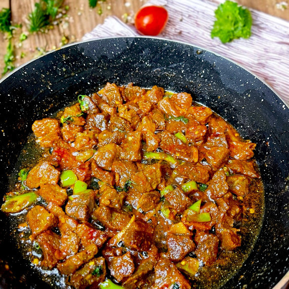 Beef stir fry arranged in black pan on wooden table 