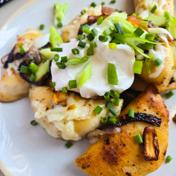 Golden pierogies with white sour cream and green onions and chives.