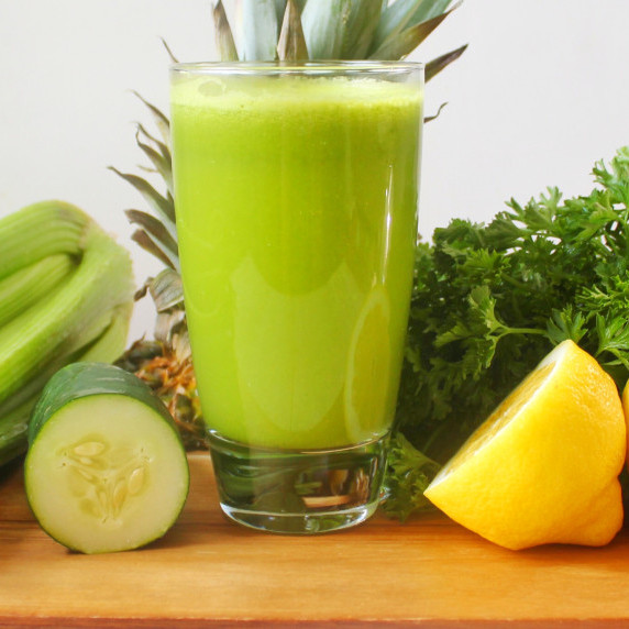 Tall glass of green juice surrounded by fruits and vegetables. 