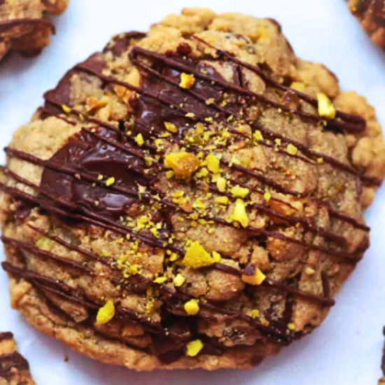 Close-up of a chewy Pistachio Chocolate Chip Cookie drizzled with dark chocolate and topped with cho