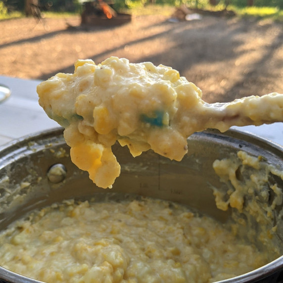 summer corn polenta being spooned from a pot with a campfire in the background