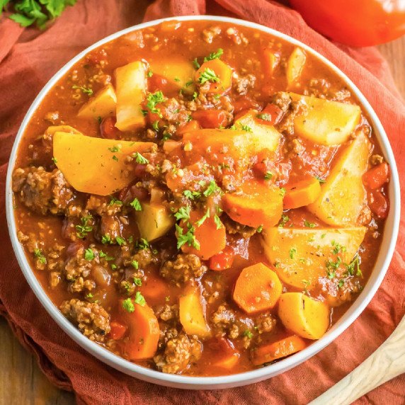 A bowl of Poor Man's Stew with ground beef, potatoes and vegetables in a bowl on a table.