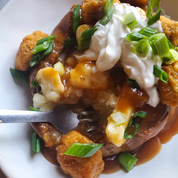 A baked potato smothered in rich, caramel coloured gravy with white sour cream and green onions.