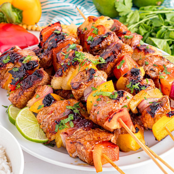 A plate of grilled pork tenderloin skewers with chunks of pork, bell peppers, pineapple, and onions.