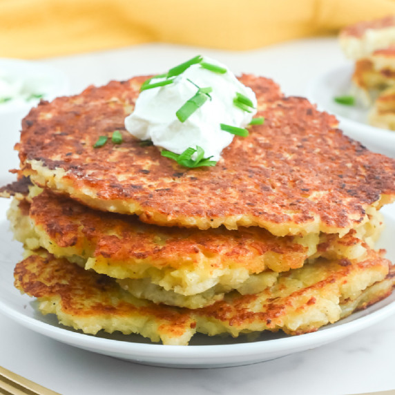 A square view of a stack of potato pancakes with sour cream and chives.