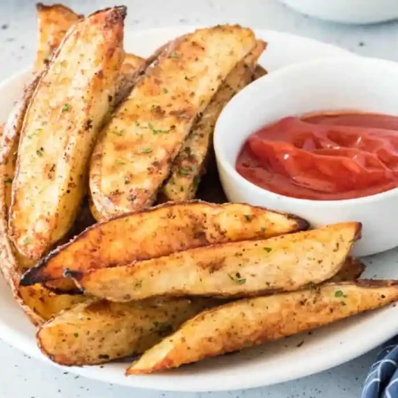 Potato wedges close up on platter with ketchup in a bowl.