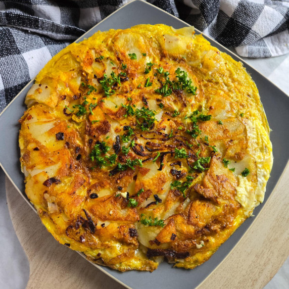 Golden brown omelet garnished with green herbs on a grey plate against a checkered towel.