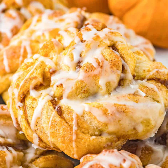 Close up of a pumpkin crescent roll twist pastry drizzled with icing.