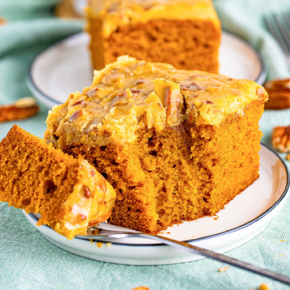 A slice of pumpkin cake on a plate with a fork missing a bite.