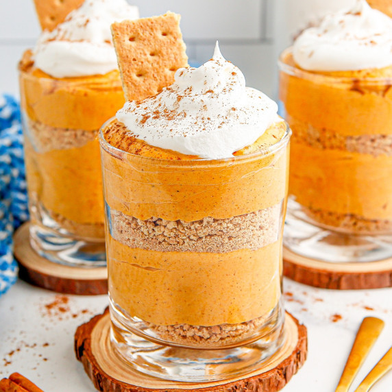 Three pumpkin pie puddings in a glass with whipped cream and graham crackers.