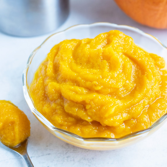 Pumpkin Puree RECIPE served in a clear bowl and with a spoon scooping out the puree.